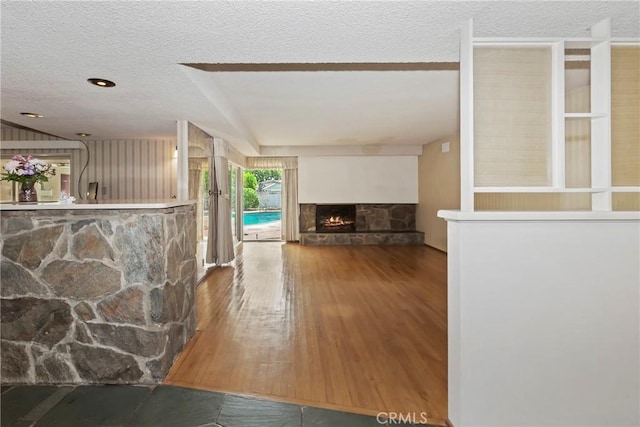 unfurnished living room featuring a textured ceiling, a stone fireplace, and wood finished floors