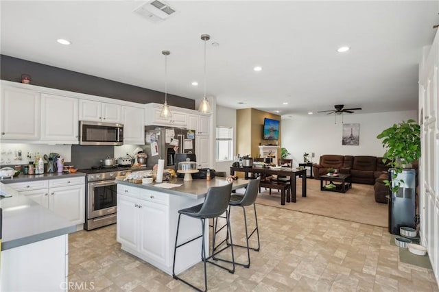 2921 Gibson St, Riverside, CA 92503 - kitchen with stainless steel appliances, a ceiling fan, a kitchen breakfast bar, white cabinets, and hanging light fixtures