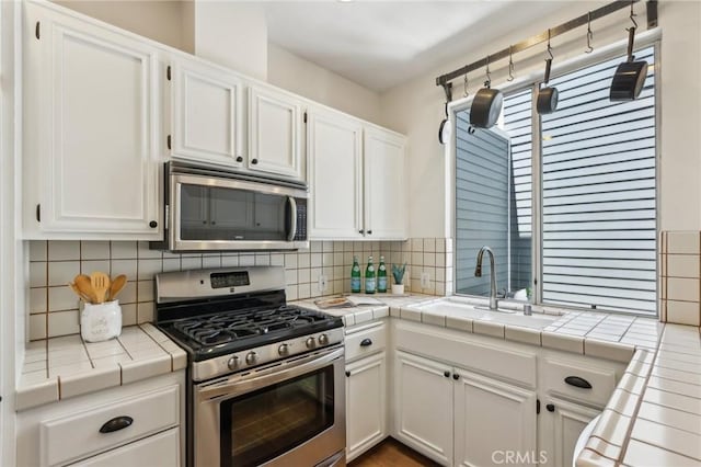 1304 12th St Unit B, Manhattan Beach, CA 90266 - kitchen with stainless steel appliances, a sink, tile counters, white cabinets, and tasteful backsplash