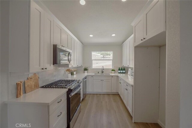 16739 Mission St, Hesperia, CA 92345 - kitchen featuring stainless steel appliances, a sink, decorative backsplash, white cabinets, and light wood-type flooring