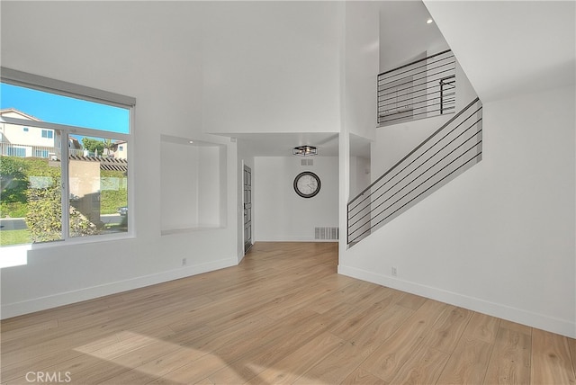 27 Burriana, San Clemente, CA 92672 - unfurnished living room featuring a towering ceiling, stairway, baseboards, and light wood-style floors