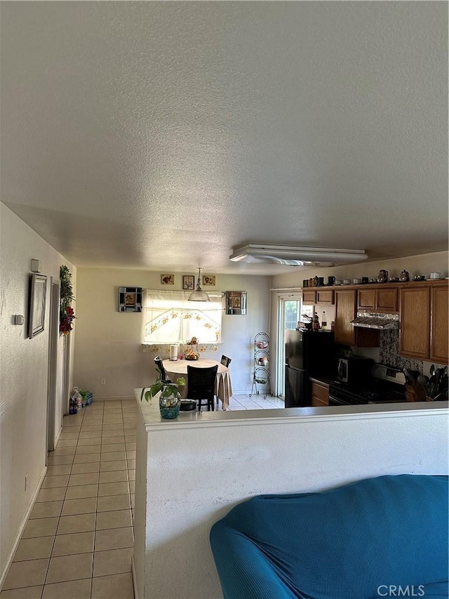 336 Pyramid Ave, Merced, CA 95341 - kitchen with electric stove, under cabinet range hood, light tile patterned floors, a textured ceiling, and brown cabinetry
