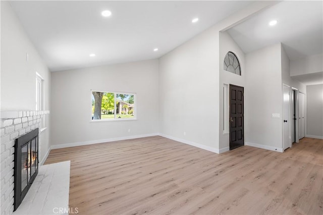 unfurnished living room featuring a fireplace, light wood-style floors, baseboards, recessed lighting, and high vaulted ceiling