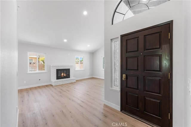 foyer entrance with light wood-style flooring, baseboards, recessed lighting, and a brick fireplace