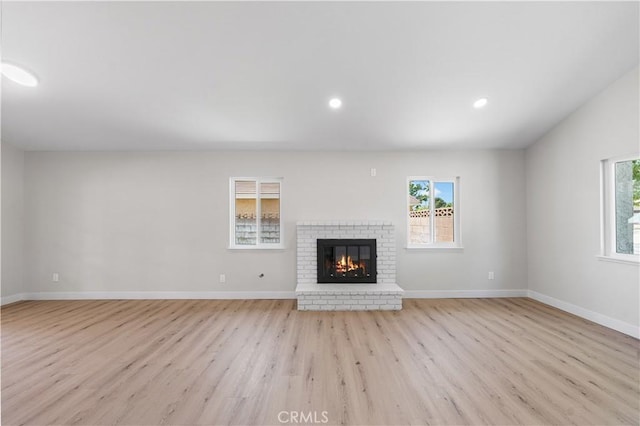 unfurnished living room with healthy amount of natural light, light wood-style floors, a fireplace, baseboards, and recessed lighting