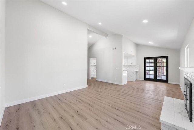unfurnished living room with lofted ceiling, a fireplace, light wood-style flooring, baseboards, and recessed lighting