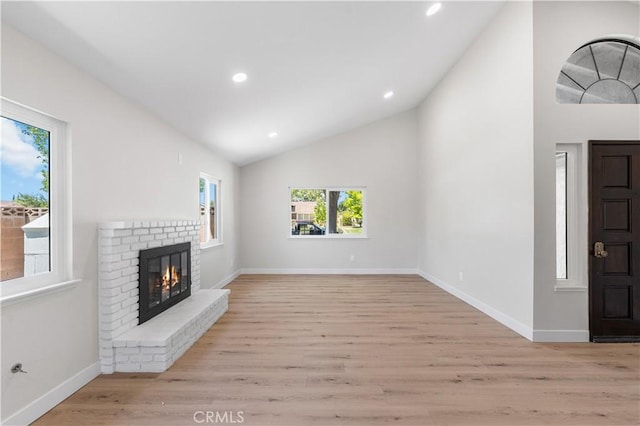 unfurnished living room with vaulted ceiling, light wood-style floors, a brick fireplace, recessed lighting, and baseboards