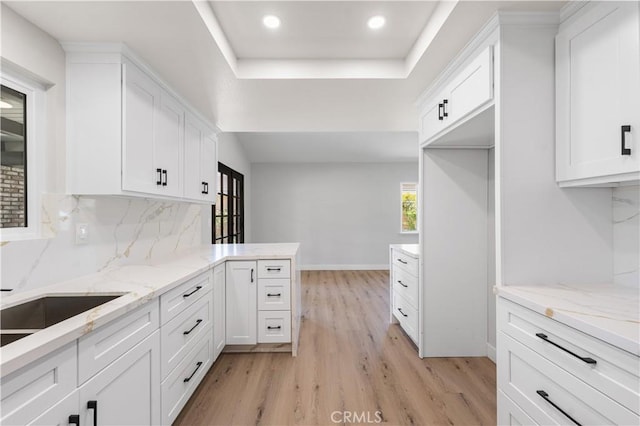 kitchen with light wood finished floors, a raised ceiling, white cabinets, recessed lighting, and decorative backsplash