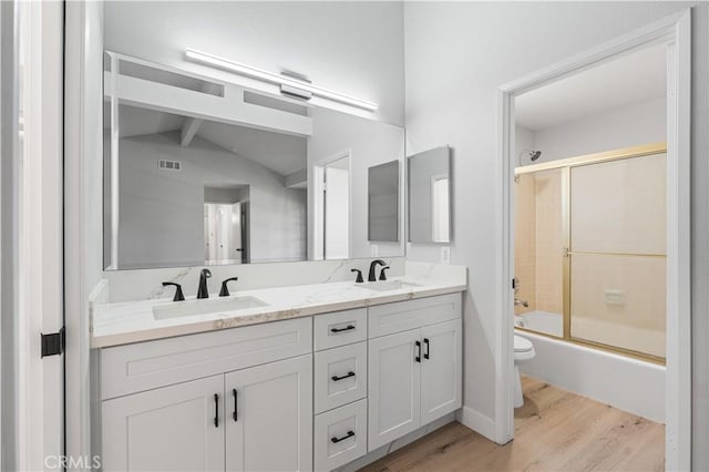 bathroom with wood finished floors, toilet, double vanity, and bath / shower combo with glass door