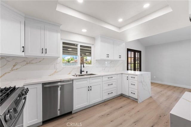 kitchen with stainless steel appliances, a sink, a peninsula, backsplash, and a tray ceiling