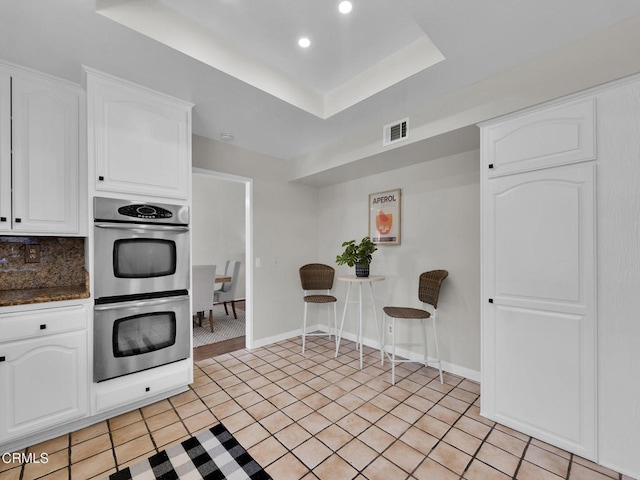kitchen with stainless steel double oven, white cabinets, recessed lighting, a tray ceiling, and tasteful backsplash