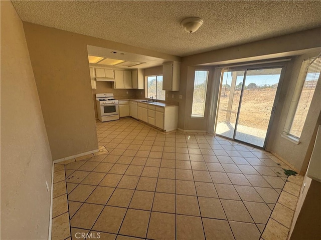 kitchen with white gas range, a sink, a textured ceiling, white cabinets, and light tile patterned floors