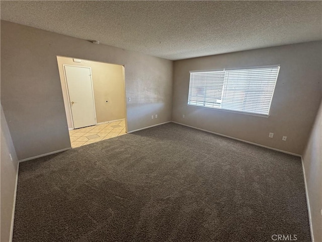 empty room with carpet, a textured ceiling, baseboards, and tile patterned floors
