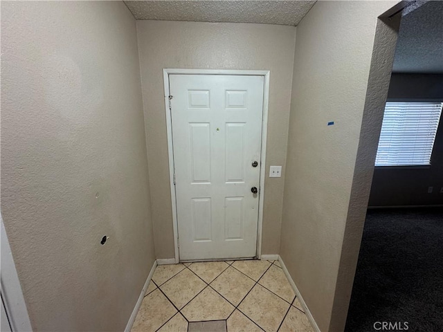 doorway featuring light tile patterned floors, a textured wall, and baseboards