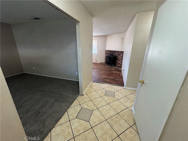 hall featuring a textured ceiling, light tile patterned floors, baseboards, and light colored carpet