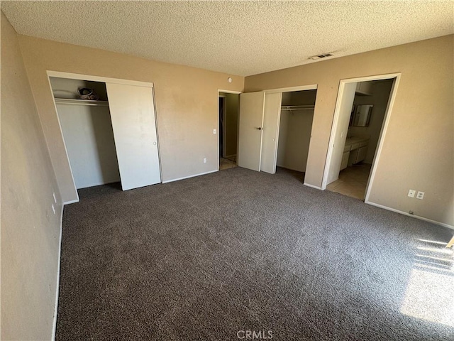 unfurnished bedroom with two closets, carpet flooring, a textured ceiling, and ensuite bath
