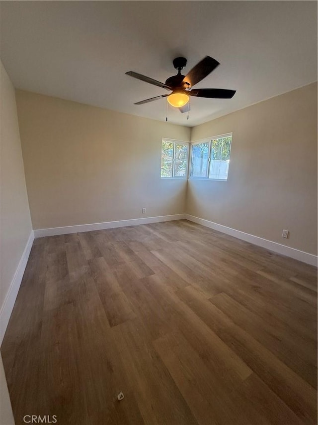 spare room with wood finished floors, a ceiling fan, and baseboards