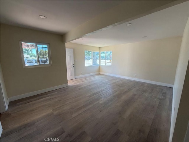 empty room with baseboards, wood finished floors, and beam ceiling