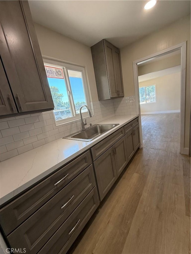 kitchen with a sink, light wood-style floors, decorative backsplash, baseboards, and light stone countertops