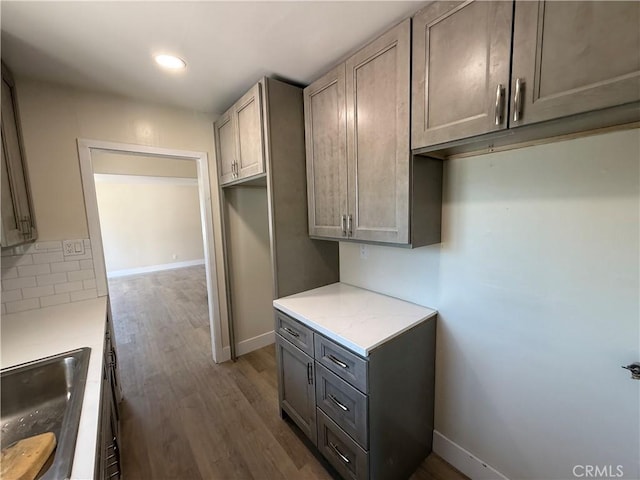 kitchen featuring baseboards, dark wood-style flooring, gray cabinetry, a sink, and recessed lighting