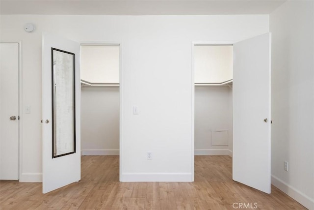 unfurnished bedroom with a spacious closet, light wood-style floors, and baseboards