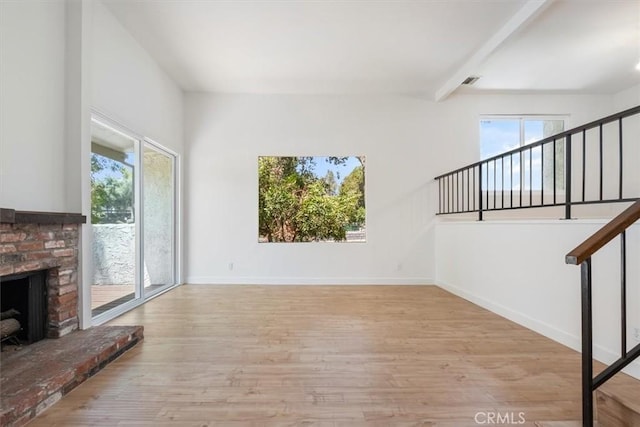 unfurnished living room featuring light wood-style floors, stairway, a brick fireplace, baseboards, and beamed ceiling
