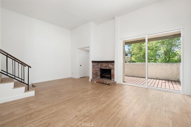 unfurnished living room with wood finished floors, a fireplace, stairs, and baseboards