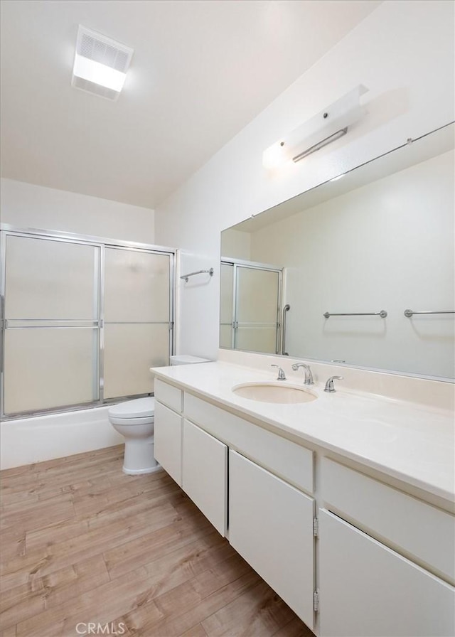 bathroom with vanity, toilet, wood finished floors, and combined bath / shower with glass door