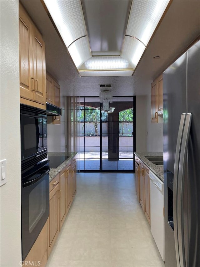 kitchen with black appliances, a tray ceiling, exhaust hood, light stone countertops, and light flooring