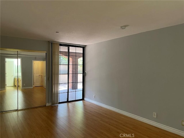 empty room with a wall of windows, wood finished floors, and baseboards