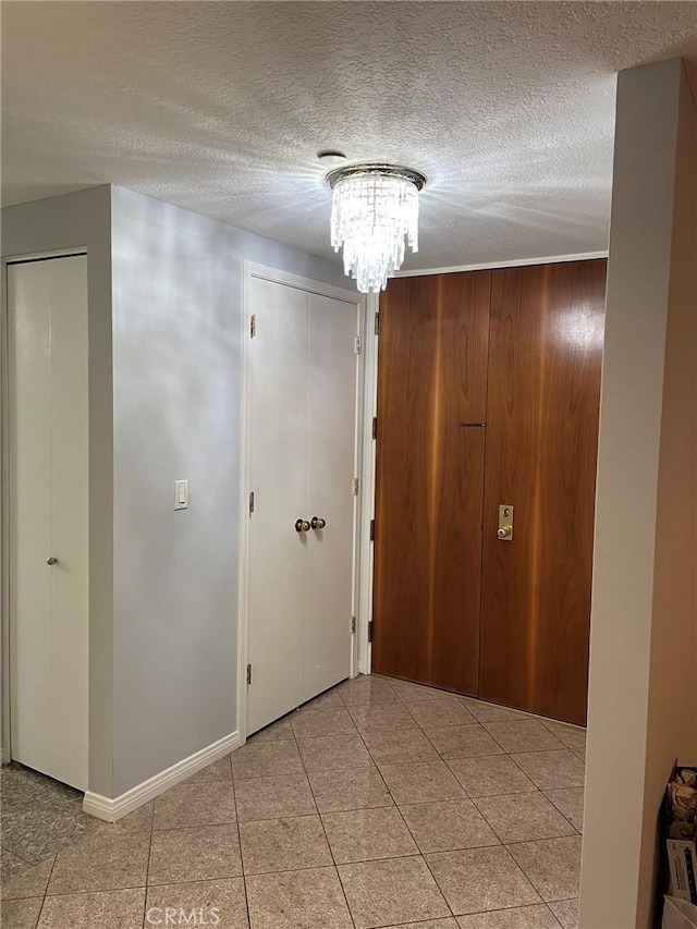 corridor featuring a textured ceiling, a chandelier, light tile patterned floors, and baseboards