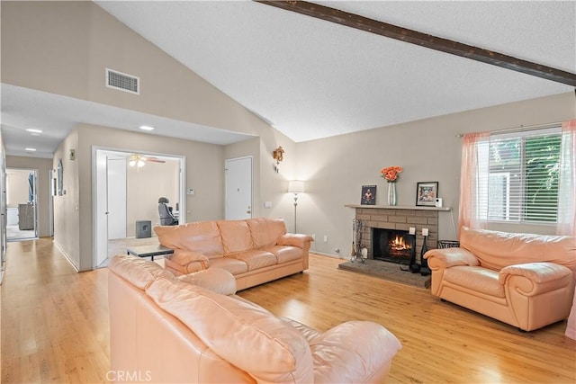 living area featuring light wood-style flooring, a brick fireplace, a ceiling fan, and a textured ceiling