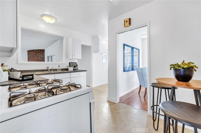 8873 Coolhurst Dr, Pico Rivera, CA 90660 - kitchen featuring white gas range oven, white cabinetry, a sink, dark countertops, and baseboards