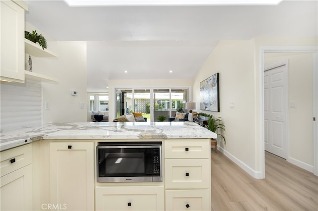 kitchen featuring built in microwave, light wood finished floors, open shelves, light stone countertops, and a peninsula