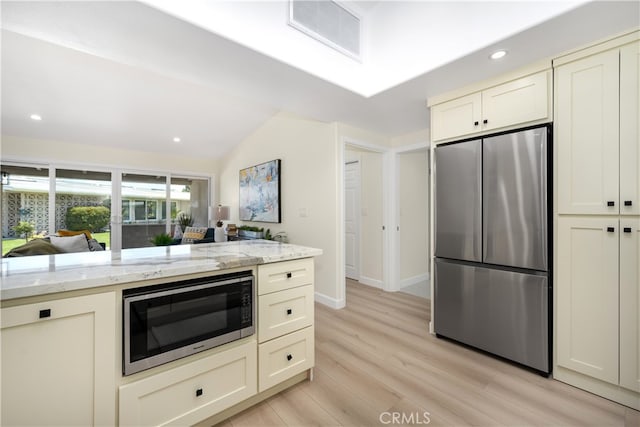 kitchen with appliances with stainless steel finishes, light wood finished floors, light stone counters, recessed lighting, and vaulted ceiling