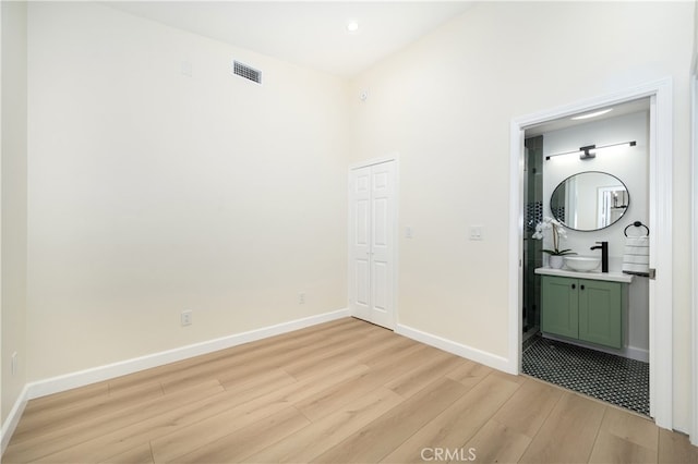 unfurnished bedroom featuring light wood-style floors, baseboards, a sink, ensuite bath, and recessed lighting