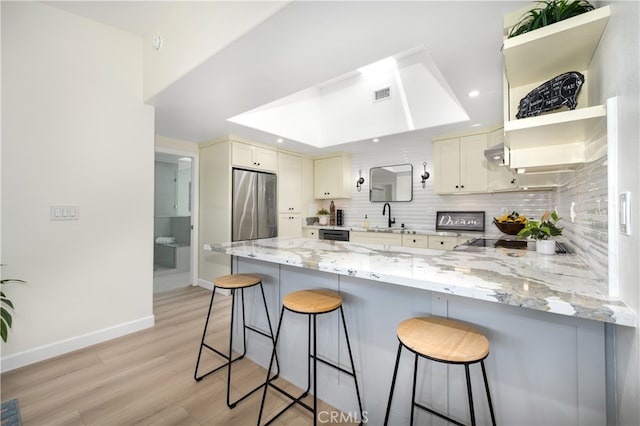 kitchen with stainless steel fridge, a peninsula, decorative backsplash, light wood finished floors, and light stone counters