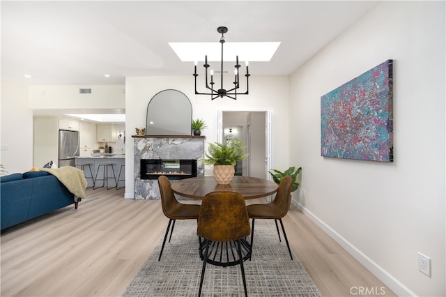 dining area with a skylight, light wood-style flooring, a high end fireplace, baseboards, and recessed lighting