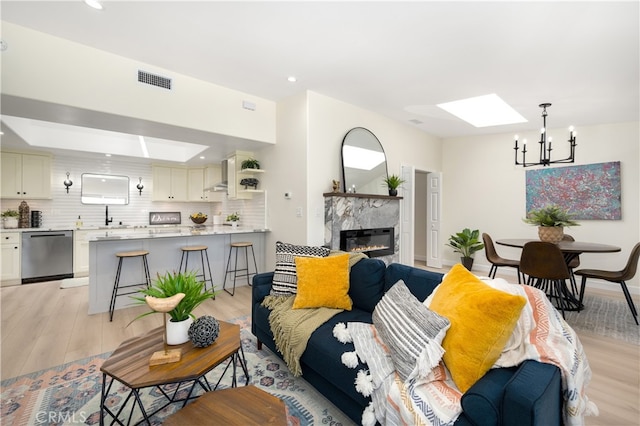living area featuring a skylight, a chandelier, light wood-style flooring, a fireplace, and recessed lighting