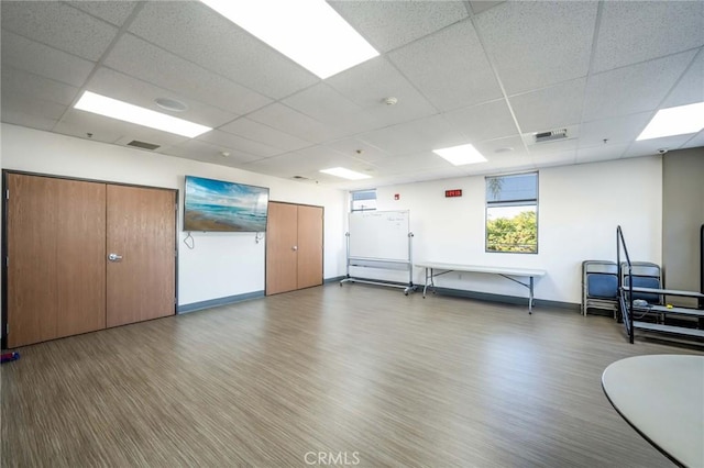 exercise room featuring a drop ceiling, light wood-style floors, and baseboards