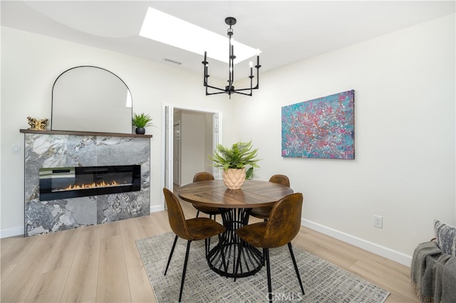 dining room featuring a chandelier, light wood-style floors, a premium fireplace, and baseboards