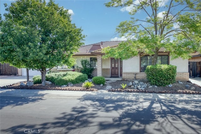 view of property hidden behind natural elements featuring driveway, stucco siding, brick siding, fence, and a tiled roof