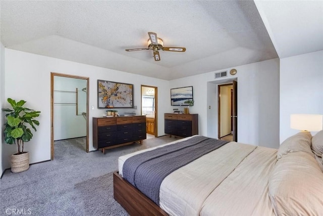 bedroom with light colored carpet, a raised ceiling, a textured ceiling, ceiling fan, and ensuite bath