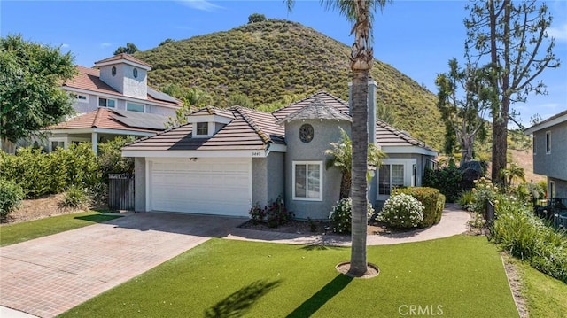 view of front of property featuring stucco siding, decorative driveway, a garage, a front yard, and a mountain view
