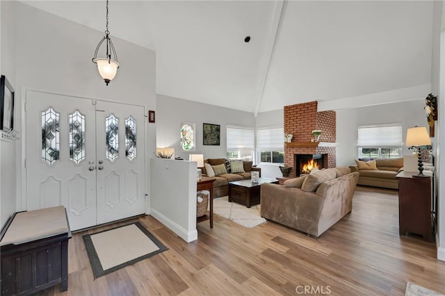 entryway with high vaulted ceiling, light wood-style floors, a fireplace, healthy amount of natural light, and baseboards