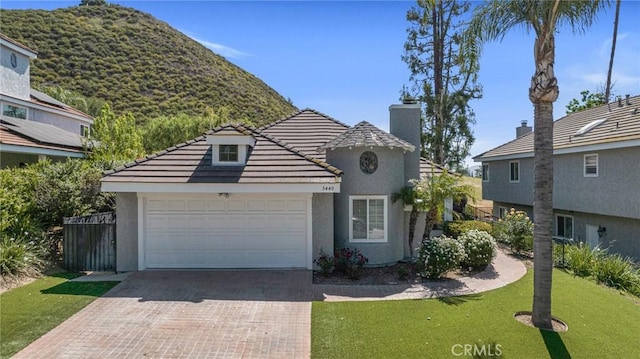 view of front of property featuring stucco siding, a chimney, decorative driveway, an attached garage, and a tiled roof