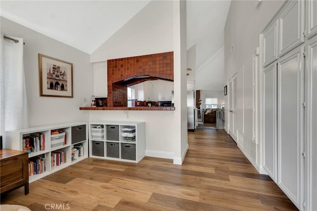 kitchen with high vaulted ceiling, light wood finished floors, and dark countertops