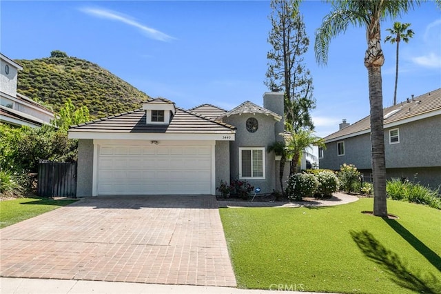 view of front of home featuring stucco siding, a garage, decorative driveway, a chimney, and a tiled roof