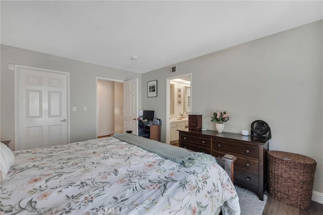 bedroom with baseboards, wood finished floors, and ensuite bath