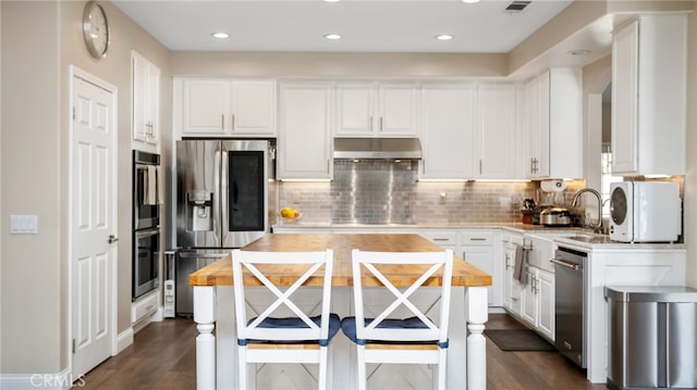 kitchen with stainless steel appliances, under cabinet range hood, white cabinetry, tasteful backsplash, and wooden counters